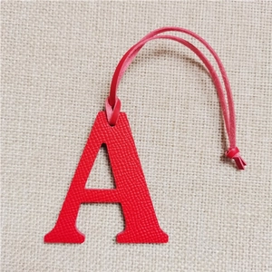 Detail shot of a red leather letter A bag charm with litchi texture on beige fabric