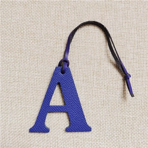 Close-up of a blue leather letter A bag charm with matching lanyard on beige linen