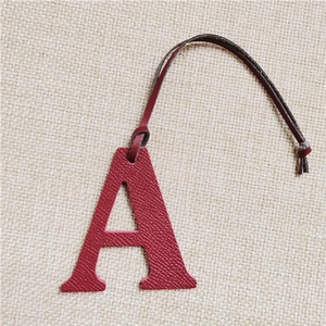 Detail of red leather letter A charm with textured finish and dark leather strap