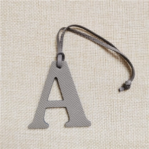Detailed view of grey Epsom leather letter A charm for handbags on linen background