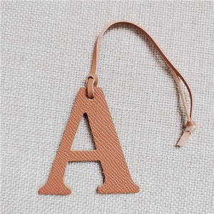 Detail view of brown leather letter A bag charm with strap on beige fabric background
