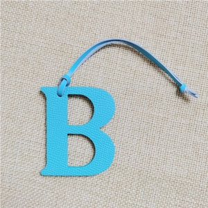 Close-up of a blue leather letter B handbag charm on a rustic burlap background