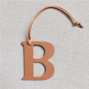 Detailed view of a brown leather letter B bag charm with strap on beige fabric