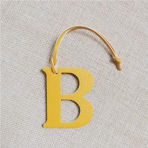 Detail view of yellow leather letter B bag charm with matching strap and visible stitching
