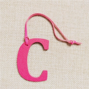 Detail of rose red letter C leather charm with litchi texture and matching lanyard