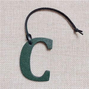 Close-up of green lychee leather letter C bag charm with a black leather lanyard