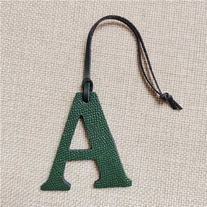 Detail view of dark green pebbled leather letter A charm with black lanyard on linen