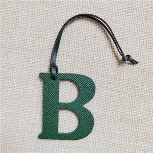 Detail view of dark green letter B bag charm with lychee pattern leather texture