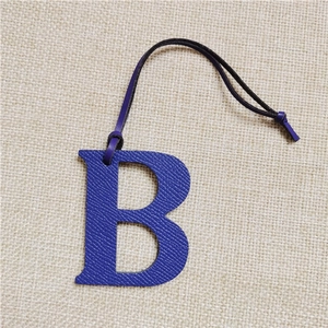 Close-up of blue leather letter B bag charm with lychee texture and black cord strap