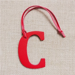 Detail of red leather letter C bag charm with litchi texture on beige linen background
