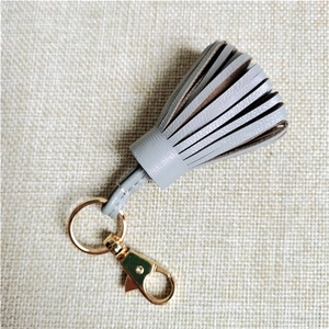 Detailed close-up of grey leather tassel keychain with polished gold metal hardware