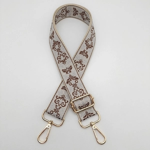 Detail of adjustable beige jacquard bag strap with brown pattern and gold metal hardware