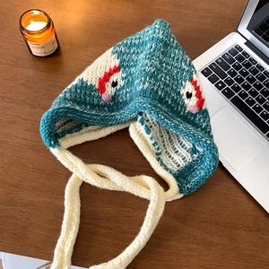 Detail of teal knit balaclava with pointed top and cozy beige drawstrings on wood background