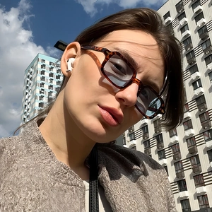 Retro tortoise frame sunglasses with light blue lenses worn by model against city sky