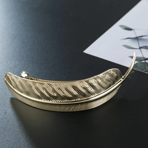 Detailed view of a metallic golden feather hair clip with intricate leaf textures on dark background