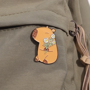 Detail of cute enamel capybara brooch with daisy on a green canvas backpack