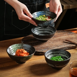 Close-up of three black ceramic bowls with assorted glaze patterns on a wooden tray