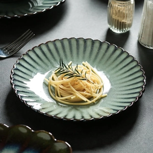 Top-down view of dark green ceramic sauce dish with retro scalloped edges and brown rim
