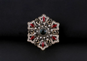 Detailed front view of a vintage Baroque star brooch with green and red crystals