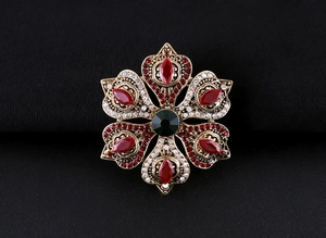 Macro detail of vintage baroque brooch featuring emerald green gem and red rhinestones