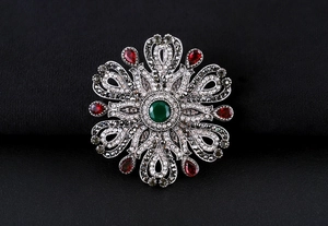Macro detail of Baroque vintage brooch with green gemstone and red crystals on black fabric