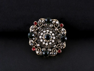 Macro detail of Baroque brooch featuring green and red crystals on gold filigree