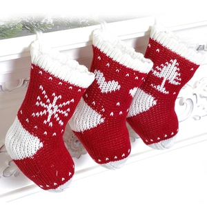 Three red knitted Christmas stockings with snowflake and heart patterns on white fireplace