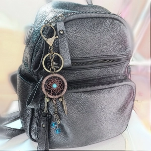 Detail of dream catcher keychain with blue feathers hanging on a dark grey leather bag