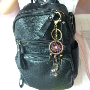Detailed view of a black pebble leather backpack with a handmade dreamcatcher feather charm