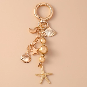 Golden keychain featuring crescent moon, seashell, and starfish charms on a pink background