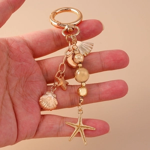 Golden keychain with starfish, shell and star pendants held by a hand on beige background