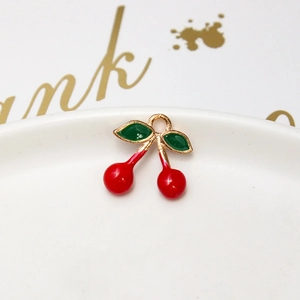 Detail of a cherry pendant with red enamel and green leaves on a white porcelain plate