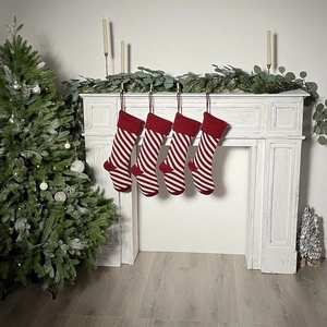 Set of four red and white striped knitted Christmas stockings hanging on a white fireplace