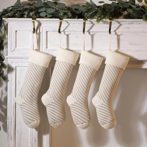 Set of four knitted Christmas stockings with beige and white stripes on a mantel