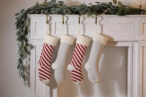 Detail of four knitted Christmas stockings in red, white and grey stripes hanging on fireplace