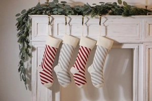 Close-up of red and grey knitted Christmas stockings hanging on a white mantel with greenery