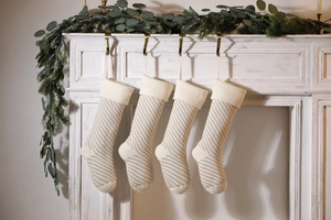 Set of 4 beige and white striped knitted Christmas stockings hanging on a white fireplace