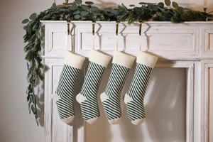 Set of four green and beige striped knitted Christmas stockings hanging on a white fireplace