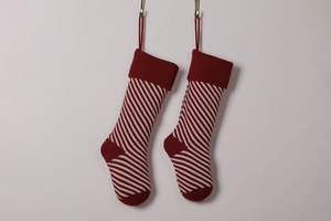 Pair of red and white striped knit Christmas stockings hanging on hooks against white wall