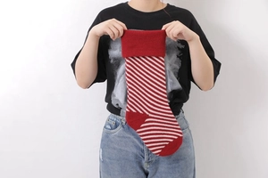 Close-up of a person holding a red and white diagonal striped knitted Christmas stocking
