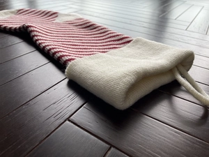 Detail of red and white striped knitted Christmas stocking with white cuff on wood