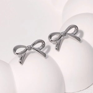 Detail view of silver bow-shaped stud earrings on a white minimalist background