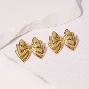 Elegant gold bow earrings with triple-layered 3D design on a white textured stone base