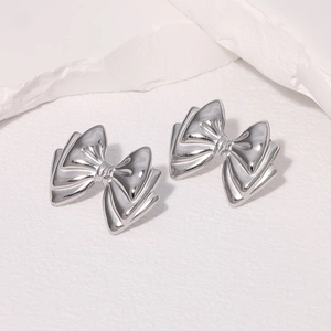 Macro detail of silver bow earrings on white textured stone with polished metallic finish