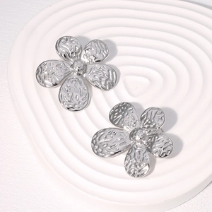 Macro detail of silver flower earrings with hammered metal texture on white tray