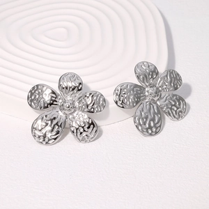 Silver flower stud earrings with hammered metal texture on white artistic pedestal
