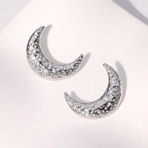 Macro shot of silver crescent earrings with a hammered metal texture and glossy finish