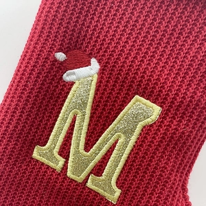Festive red knitted Christmas stocking with gold glitter letter M and Santa hat detail