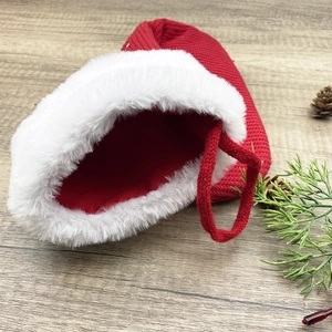 Red knit Christmas stocking with white plush trim and festive pine cone decor on wood