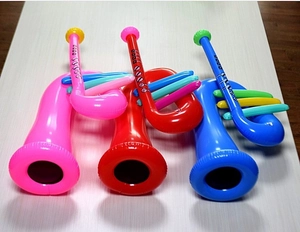 Three inflatable PVC saxophones in pink, red, and blue displayed on a light wood surface